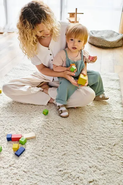 Bouclé mère et tout-petit fille lien sur Montessori bloc jouer, créer, empiler, et explorer ensemble sur le sol. — Photo de stock