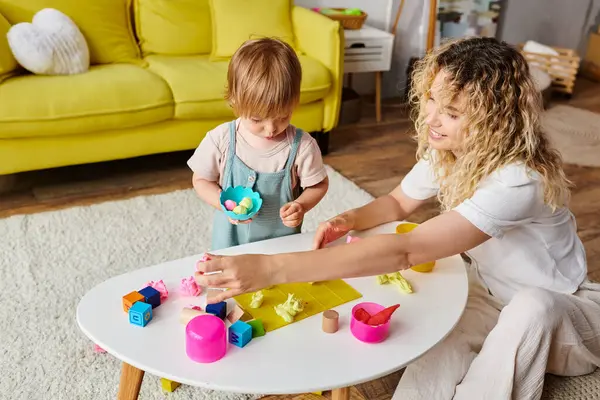 A loving mother plays with her curly toddler daughter in a warm living room, engaging in Montessori educational activities. — Stock Photo