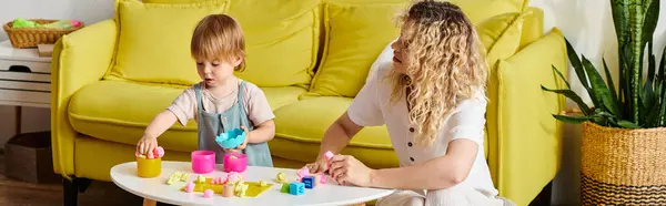 Lockige Mutter und ihre kleine Tochter üben Montessori-Unterricht aus, indem sie mit Klötzen auf einem Tisch spielen. — Stockfoto