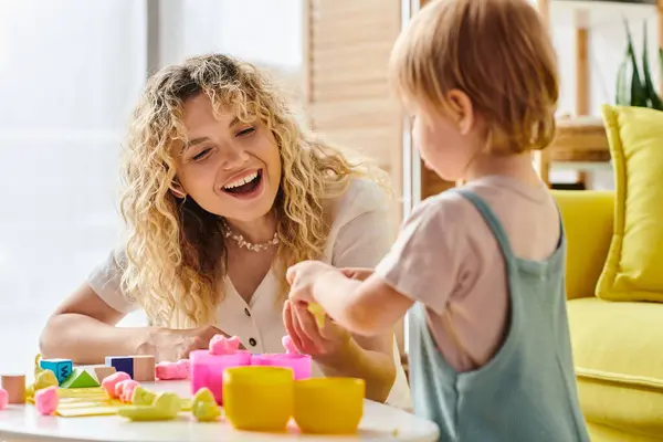 A woman with curly hair interacts with her toddler daughter using Montessori methods at a table. — Stock Photo