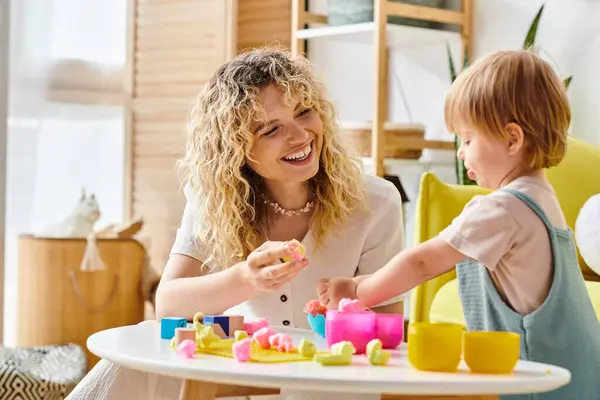 Eine Mutter mit lockigem Haar und ihre kleine Tochter nach Montessori-Pädagogik spielen gemeinsam an einem Tisch. — Stockfoto