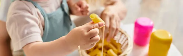 A curly-haired toddler joyfully plays with dry pasta, exploring textures and shapes in a Montessori-inspired learning moment. — Stock Photo