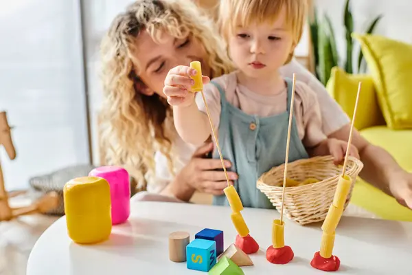 A curly mother and her toddler daughter playfully engaging with Montessori toys, fostering hands-on learning and creativity. — Stock Photo