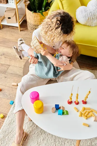 Eine Mutter und ihre Tochter spielen fröhlich mit trockener Pasta in einem gemütlichen Wohnzimmer voller Montessori-Unterrichtsmaterialien. — Stockfoto