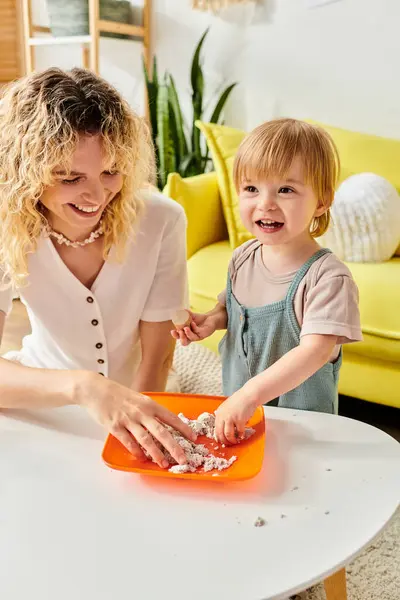 Lockige Mutter und kleine Tochter lernen spielerisch mit einer orangefarbenen Schale und umarmen die Montessori-Methode zu Hause. — Stockfoto