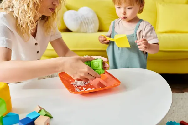 A curly-haired mother engages her toddler daughter in Montessori play, fostering learning and joy in their cozy living room. — Stock Photo