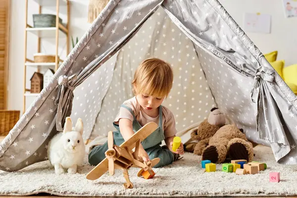Bambina gioca felicemente con i giocattoli all'interno di una tenda giocosa a casa. — Foto stock