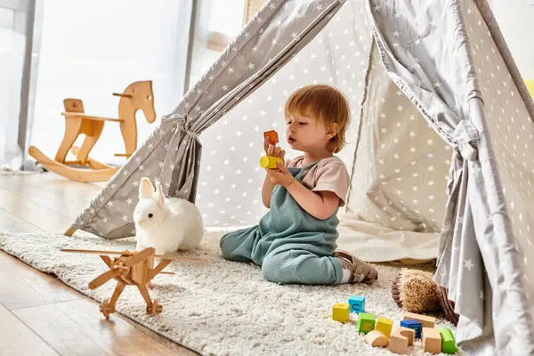Маленька дитина, занурена в гру з іграшками всередині яскравого ігрового намету, використовуючи метод Монтессорі. — стокове фото