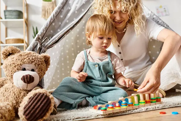 A curly-haired mother is actively playing and learning with her toddler daughter on the floor at home using the Montessori method. — Stock Photo