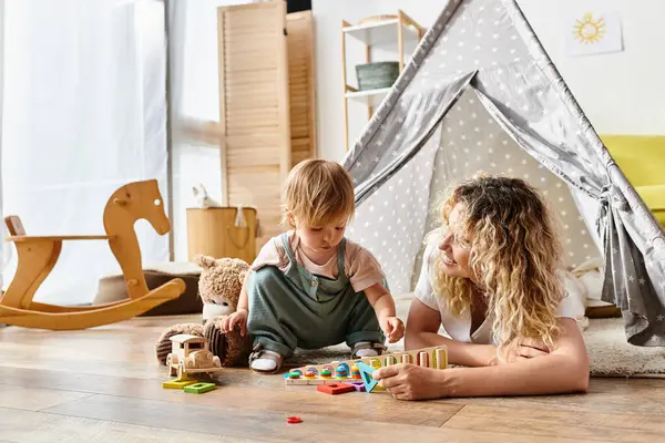 Кучерява мати та її дочка-малюк займаються уявною грою з освітніми іграшками, слідуючи методу Монтессорі. — стокове фото
