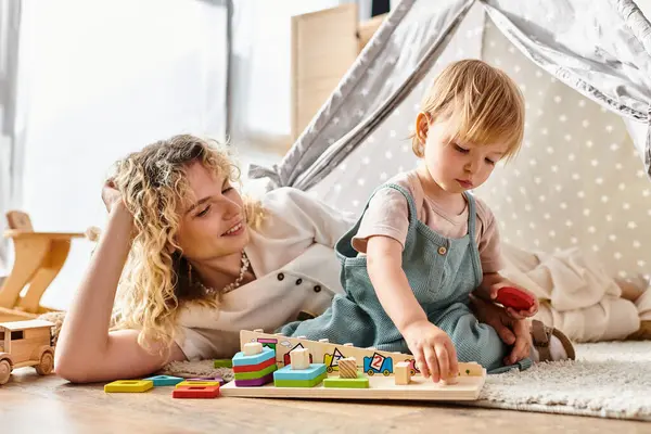 Eine lockige Mutter und ihre kleine Tochter spielen zu Hause fröhlich mit Lernspielzeug nach Montessori-Methode. — Stockfoto