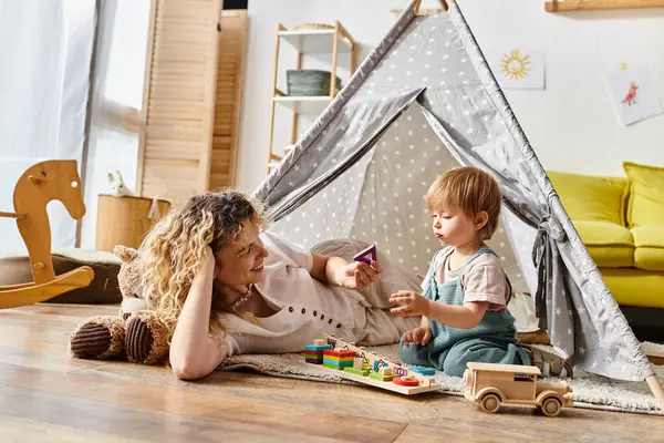 Mère bouclée et fille tout-petit jouant joyeusement ensemble dans une tente de jeu colorée, embrassant la méthode d'éducation Montessori à la maison. — Photo de stock