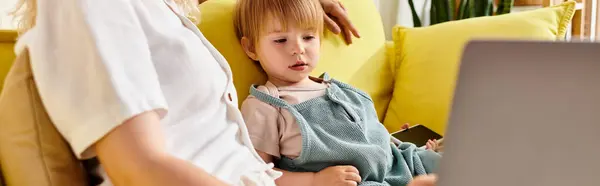 A little girl with curly hair sits on a couch, engrossed in using a laptop. — Stock Photo