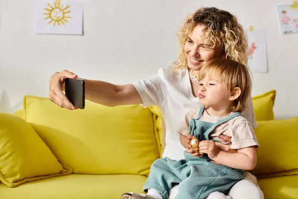 Une mère aux cheveux bouclés et sa petite fille assise confortablement ensemble sur un canapé à la maison. — Photo de stock