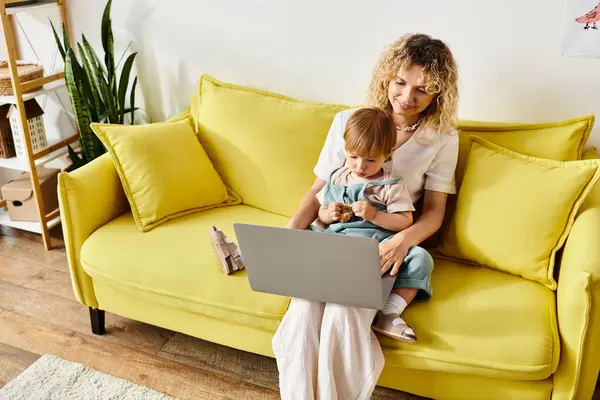 A curly-haired mother sitting on a couch, embracing her toddler daughter in a warm and loving moment at home. — Stock Photo