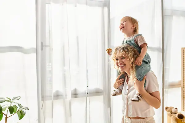 A curly-haired mother tenderly holds her toddler daughter in her arms, expressing love and care at home. — Stock Photo
