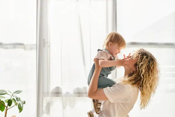 Curly mother tenderly embraces her toddler daughter at home, showcasing a beautiful bond of love and care. — Stock Photo