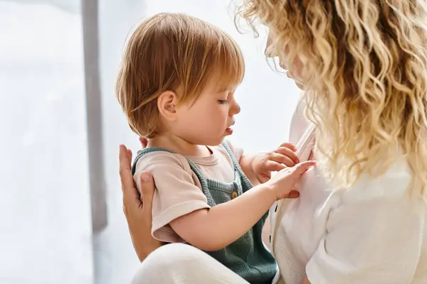 A curly-haired mother lovingly cradles her toddler daughter in her arms at home. — Stock Photo