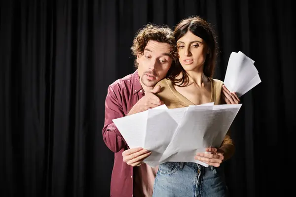 Un hombre y una mujer sosteniendo papeles frente a un fondo negro. - foto de stock