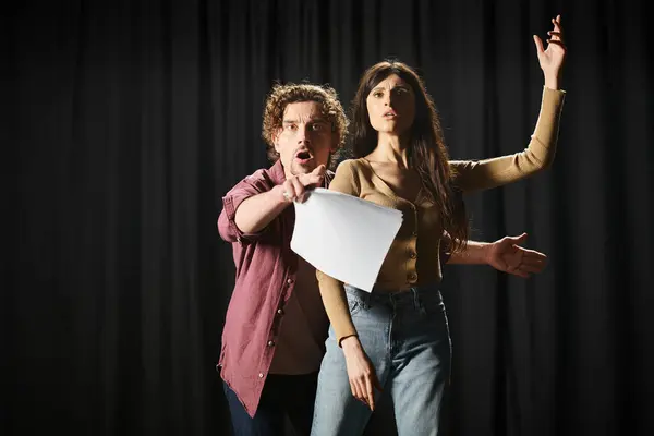 Stylish man and woman pose on stage by black backdrop. — Stock Photo