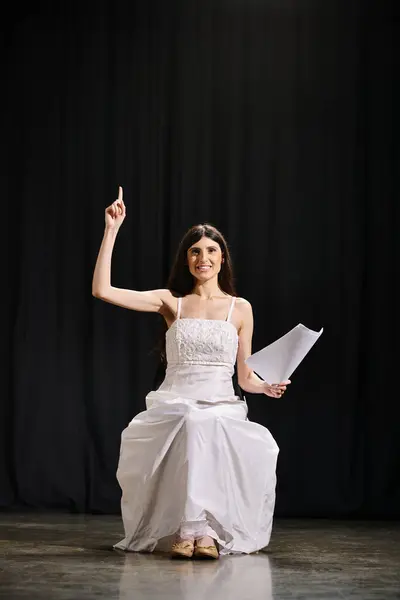 Elegante donna in abito bianco siede con grazia sul palco durante le prove. — Foto stock