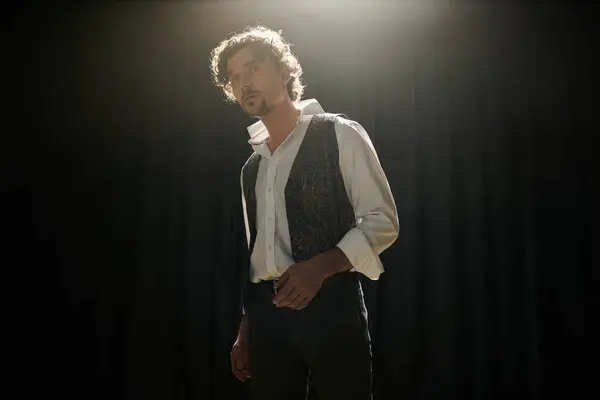 A handsome man stands confidently in front of a black curtain during a theater rehearsal. — Stock Photo