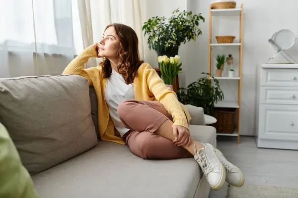 Middle aged woman sitting on a cozy couch in a stylish living room. — Stock Photo