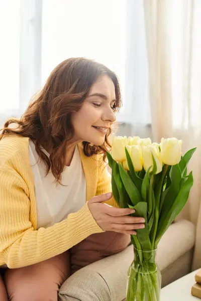 Donna di mezza età godendo di fiori sul divano. — Foto stock