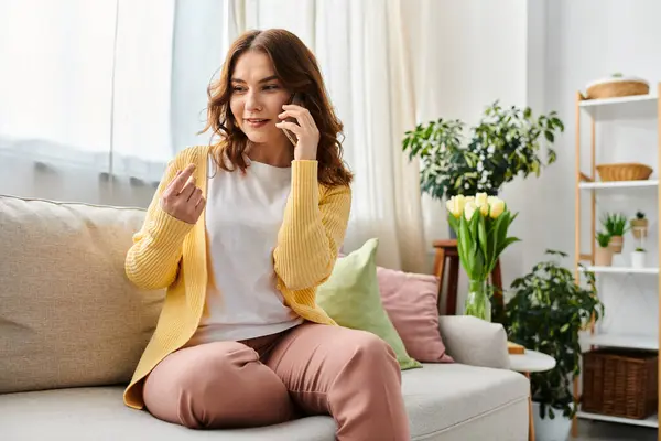 Donna di mezza età seduta sul divano, impegnata in una telefonata. — Foto stock