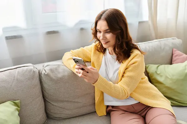 A middle-aged woman sitting on a couch, engrossed in her cell phone. — Stock Photo