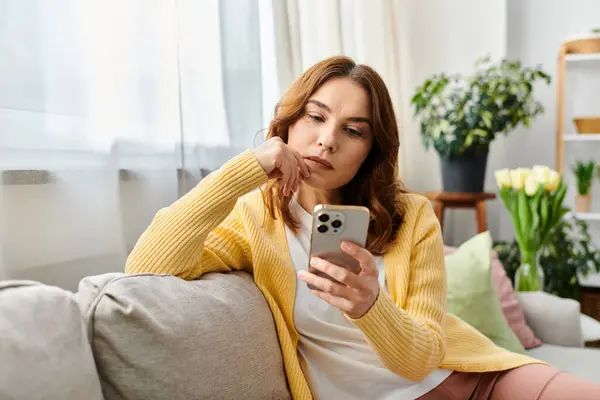 Eine Frau sitzt auf einer Couch, in ihr Handy vertieft. — Stockfoto