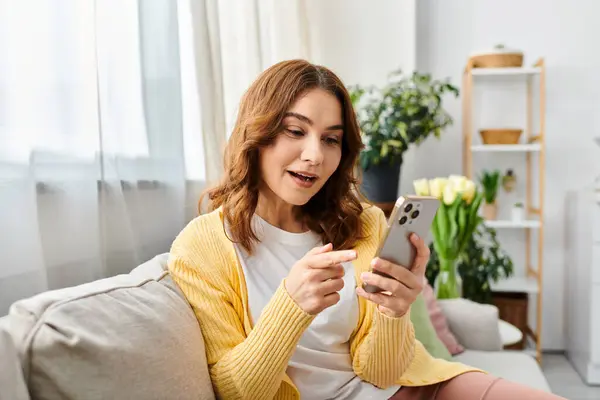 Middle aged woman engrossed in smartphone on couch. — Stock Photo