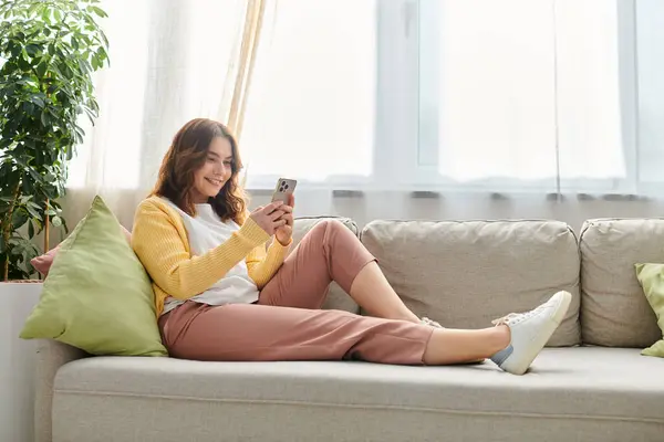 A middle aged woman lost in her cell phone on a cozy couch. — Stock Photo
