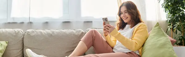 Femme d'âge moyen sur le canapé absorbé dans le téléphone portable. — Photo de stock