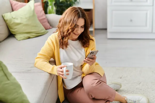 Eine Frau mittleren Alters in ihr Handy vertieft, während sie auf einer Couch sitzt. — Stockfoto