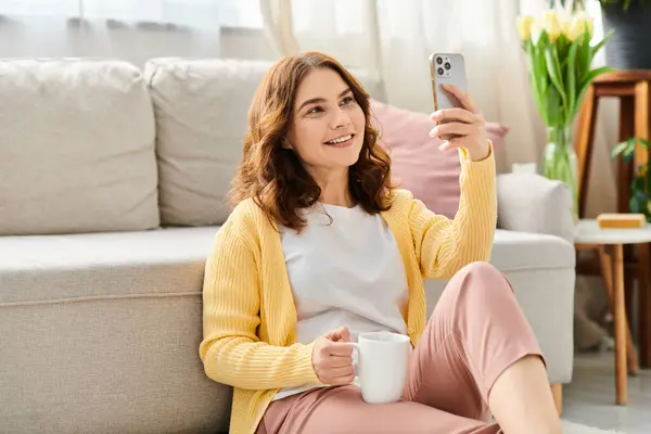 Une femme d'âge mûr s'assoit sur un canapé, prenant un selfie avec son téléphone. — Photo de stock