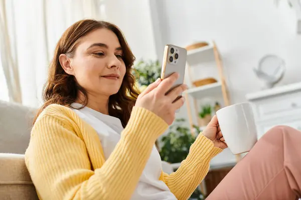 Middle aged woman relaxed on couch, focused on smartphone screen. — Stock Photo