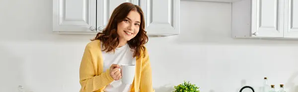 Middle-aged woman in yellow cardigan standing gracefully in kitchen. — Stock Photo