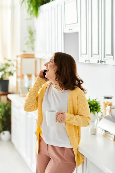 Middle aged woman standing in kitchen, chatting on cell phone. — Stock Photo