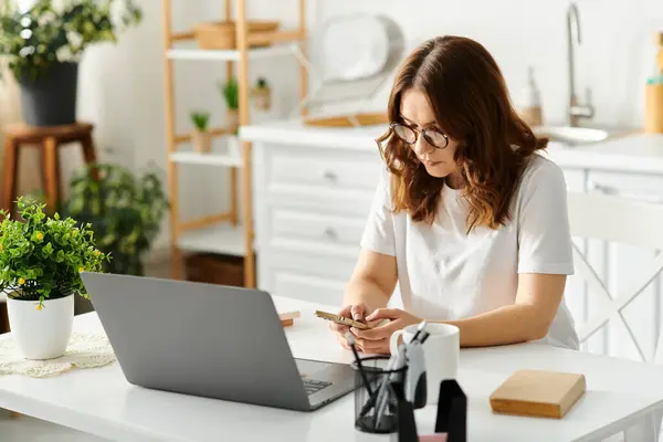 A middle-aged woman sitting at a table, engrossed in using a laptop computer. — Stock Photo