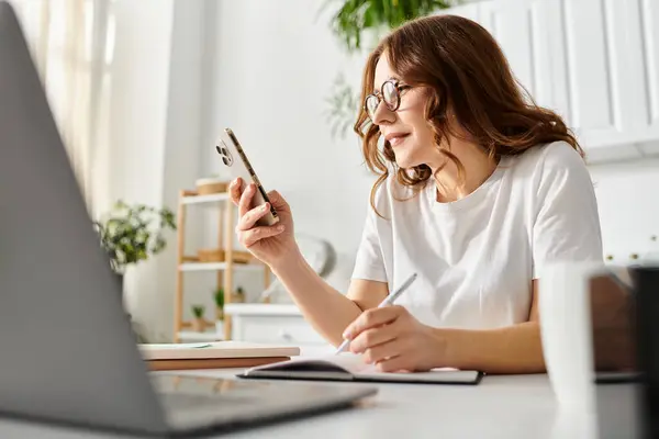 Middle aged woman sitting at desk, engrossed in cell phone use. — Stock Photo