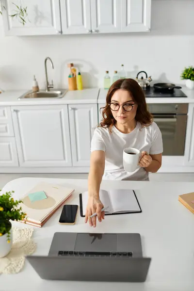 Middle aged woman working on a laptop at a kitchen table. — Stock Photo