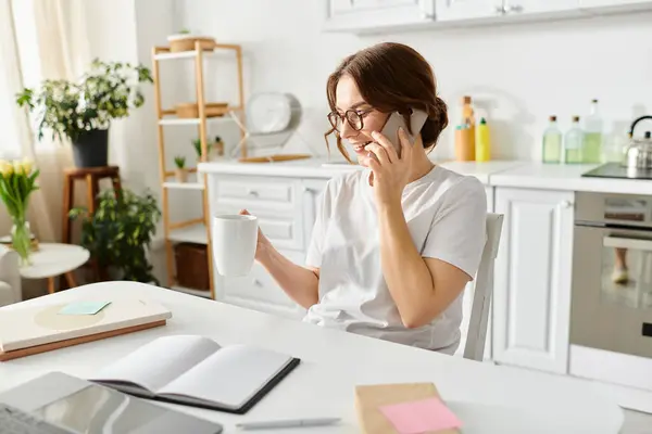 Una mujer de mediana edad sentada en una mesa, conversando por teléfono. - foto de stock