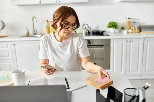 Frau mittleren Alters am Küchentisch in ihr Handy vertieft. — Stockfoto