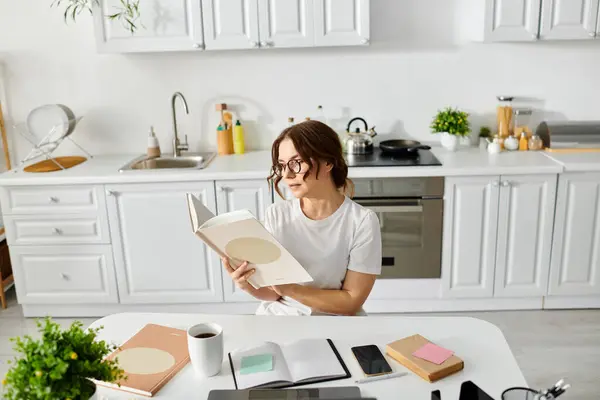 A middle-aged woman engrossed in a book at her kitchen table. — Stock Photo
