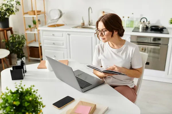Frau mittleren Alters vertieft in die Arbeit, am Tisch mit Laptop sitzend. — Stockfoto