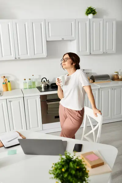 Middle-aged lady standing by table in kitchen. — Stock Photo