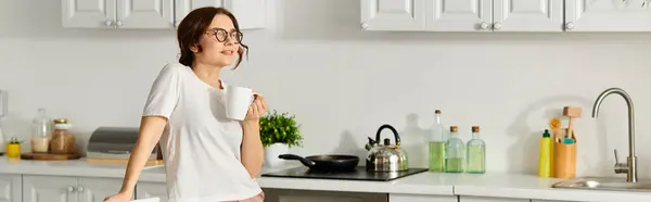 Жінка середнього віку насолоджується чашкою кави на своїй кухні. — стокове фото