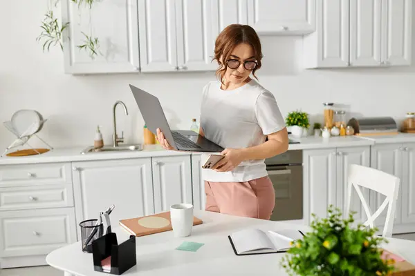 Frau mittleren Alters hält Laptop in moderner Küche. — Stockfoto