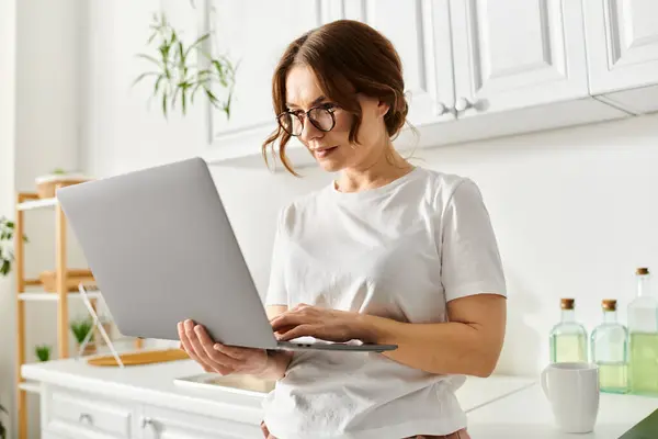 Donna di mezza età che utilizza il computer portatile in cucina. — Foto stock